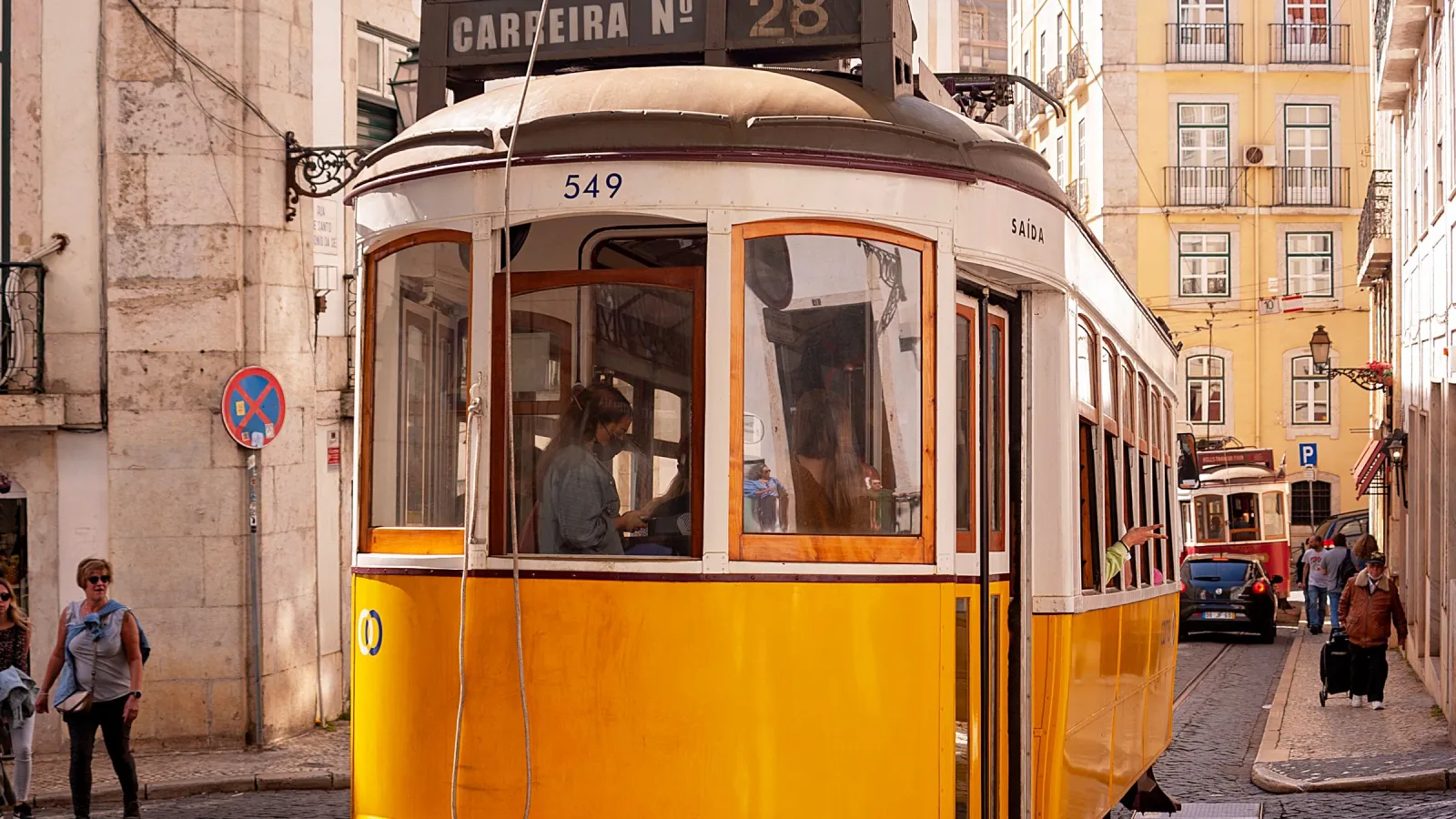 Żółty tramwaj jadący ulicą historycznej dzielnicy Lizbony